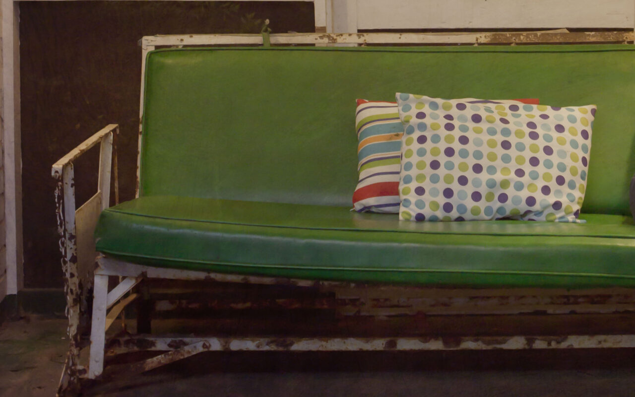 A green porch glider with patterned pillows on a Mississippi front porch